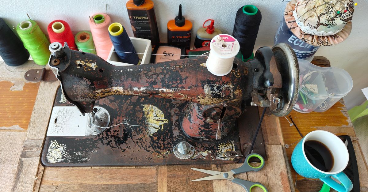 Máquina de coser doméstica sobre una mesa de madera con carretes de hilo y tijeras